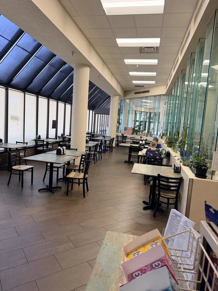 The cafe dining room: rustic wood tables and black chairs along a wall of atrium glass, columns and skylights