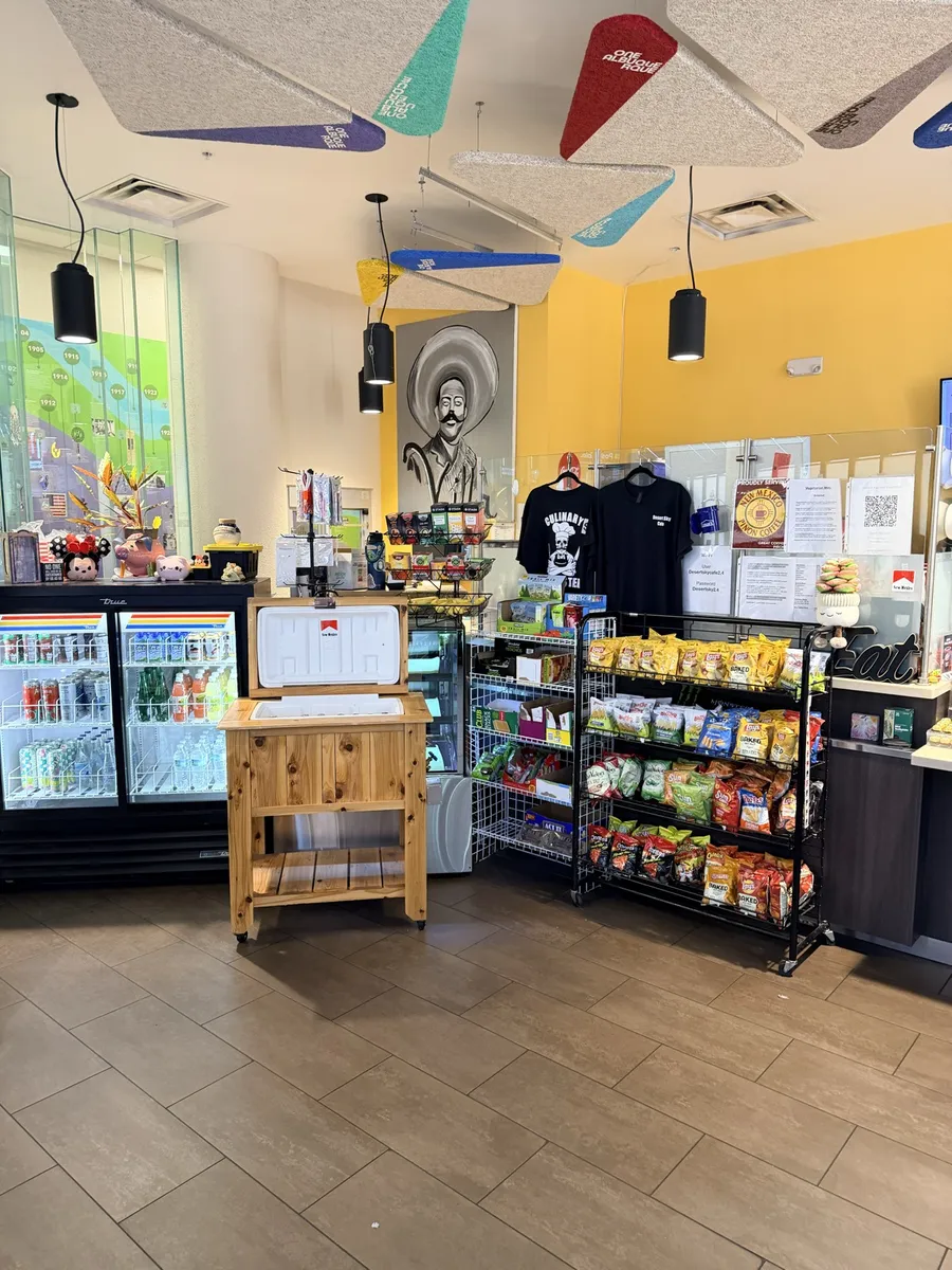 The snack and drinks corner: coolers, snack racks and shirts under yellow walls and papel picado ceiling flags
