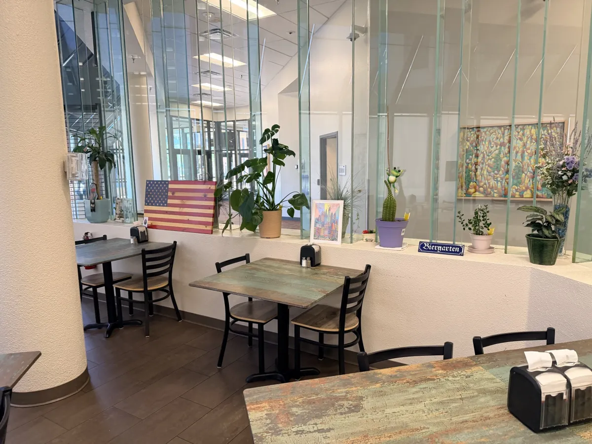 Cafe tables along the atrium glass, with plants, a wooden American flag and a Biergarten sign on the ledge